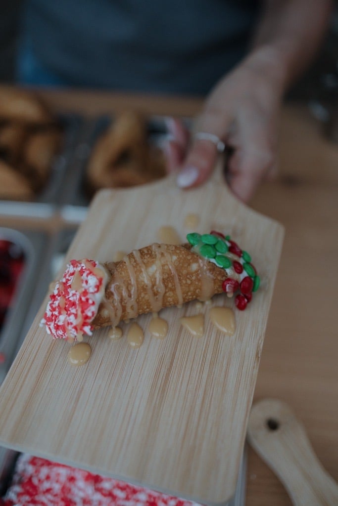Decorated cookie caterpillar with red and green sprinkles on wooden board during holiday baking