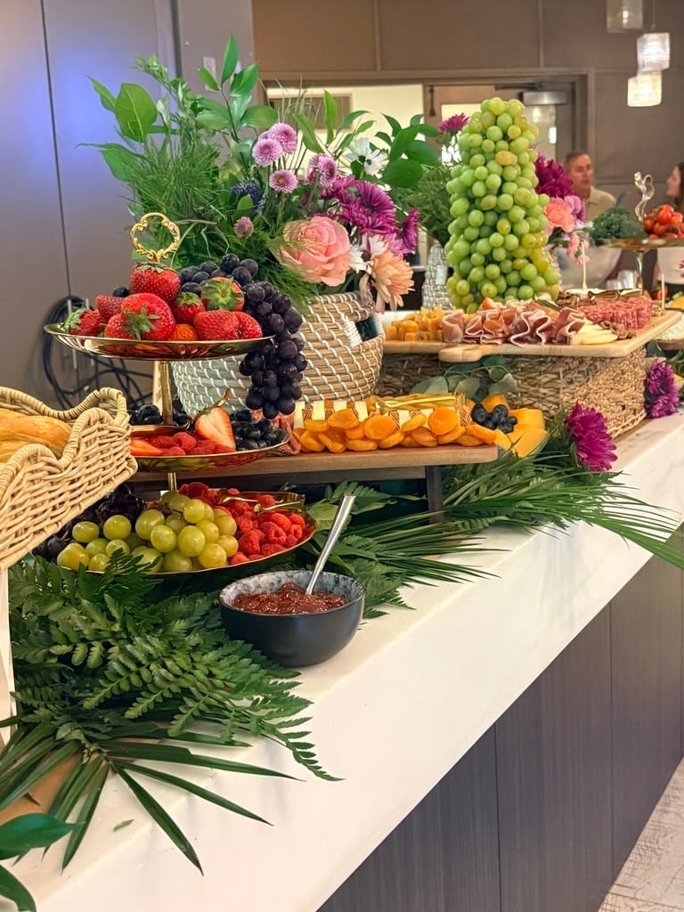 Elegant fruit and flower display with berries, citrus, grapes, and colorful blooms arranged on tiered white tables