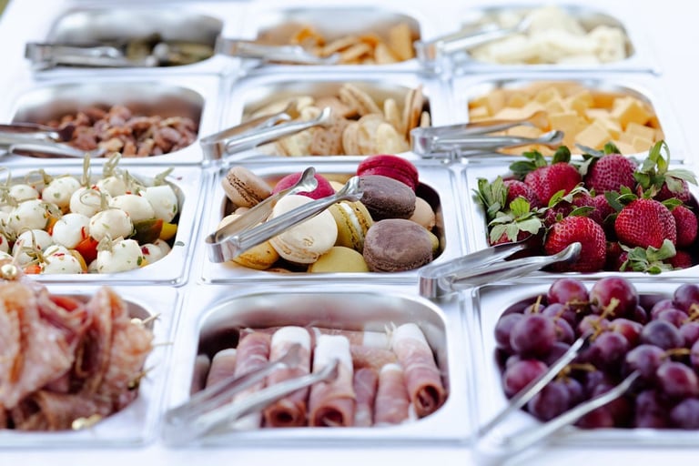 Overhead view of clear containers displaying an array of charcuterie items including cured meats, cheeses, nuts, fresh berries, and various snacks arranged in a grid.